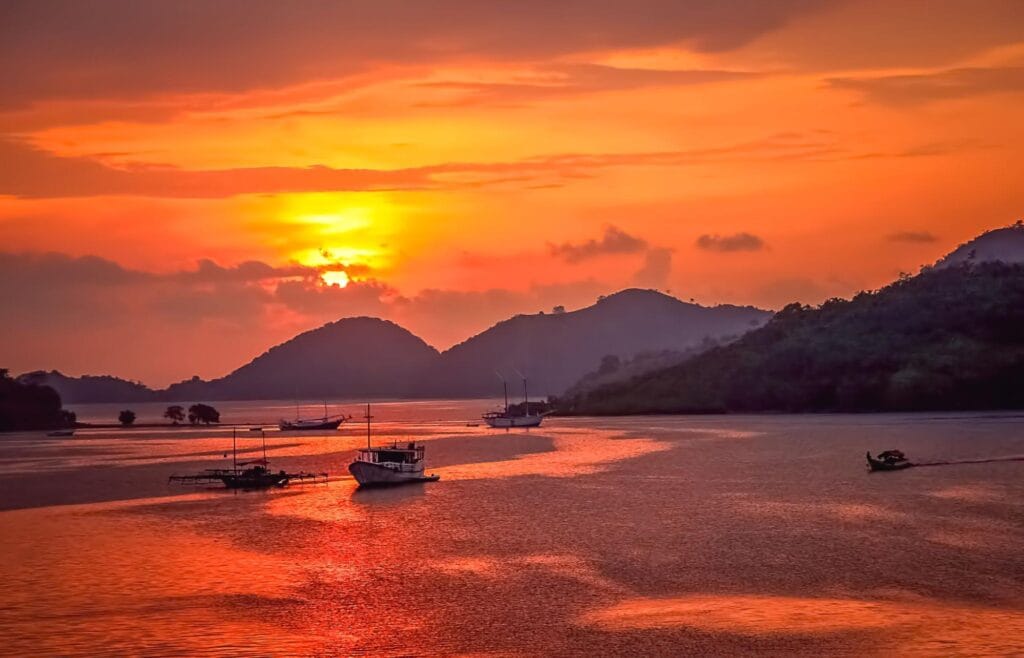 Suasana sunset di Pulau Padar dengan langit jingga dan kapal wisata di perairan